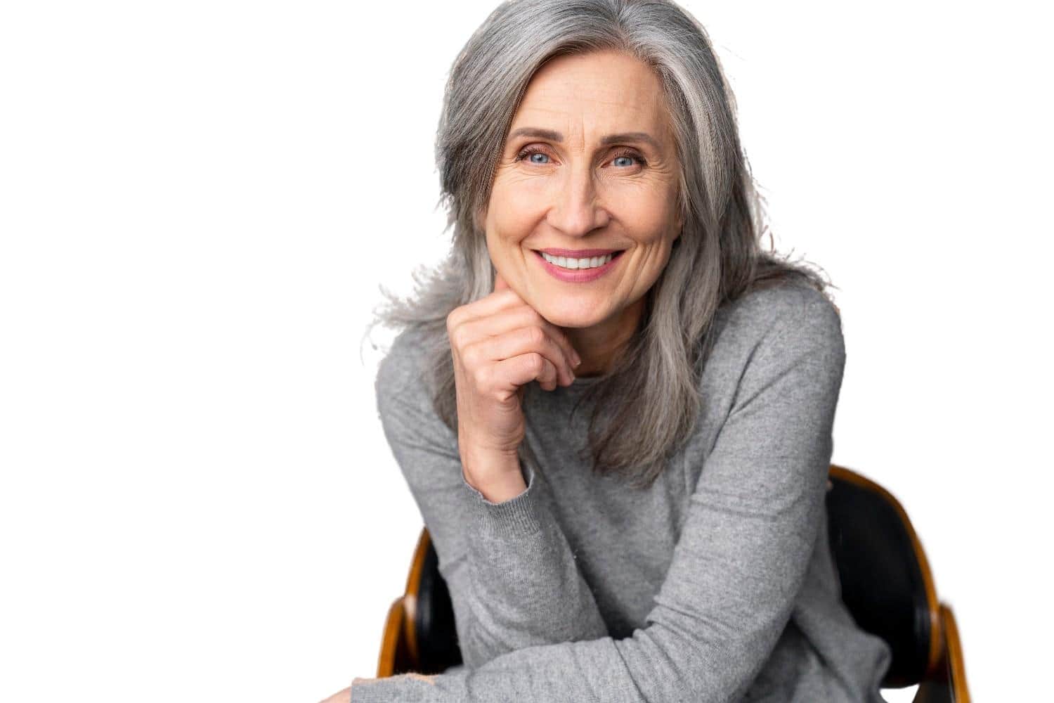 Smiling woman with gray hair in a gray sweater, sitting and posing against a white background.