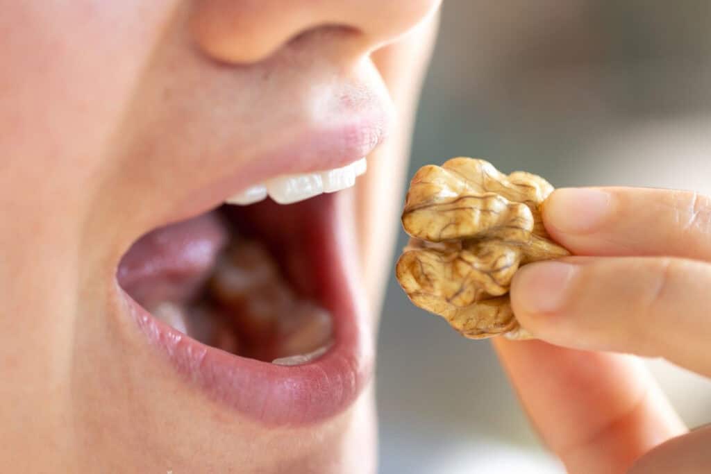 Gros plan d'une personne mangeant une noix, mettant en évidence les habitudes saines de grignotage des fruits à coque.