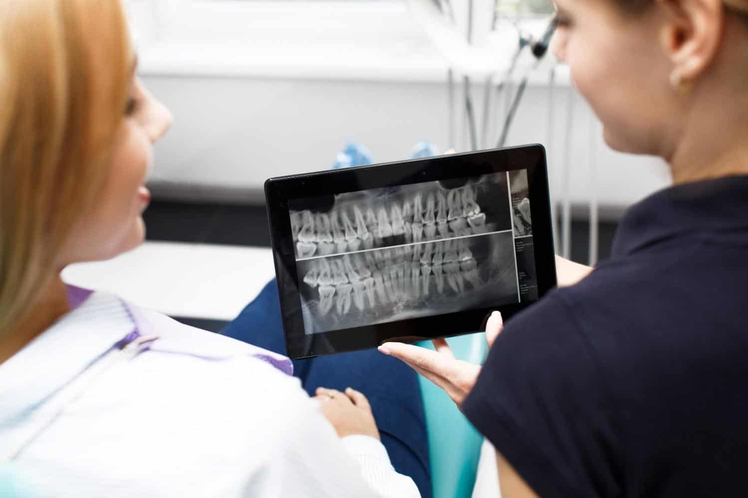 Dentista che mostra una radiografia dentale su un tablet a un paziente in una clinica.