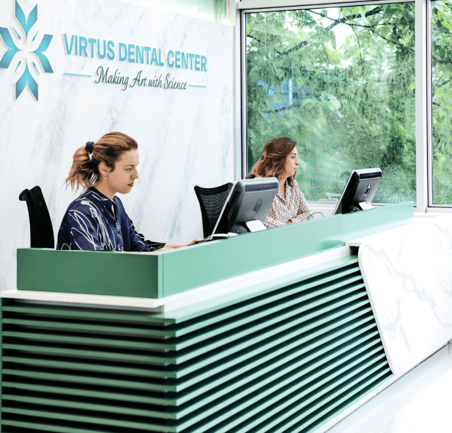 Reception del centro odontoiatrico con due membri del personale al computer, interni moderni e ampia finestra per la luce naturale.