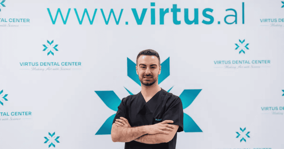 Dentist in black scrubs smiling at Virtus Dental Center, with website and logo in the background.