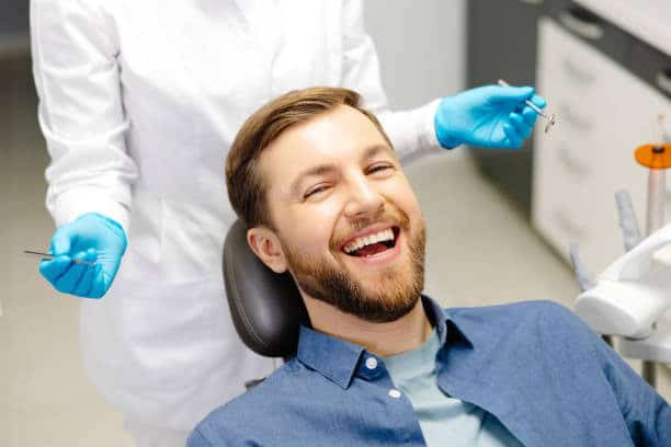 Man smiling in dental chair with dentist; happy patient during checkup in modern clinic.