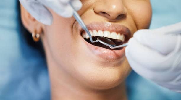 Pacienti në zyrën e stomatologut duke iu nënshtruar kontrollit dentar me pasqyrë dhe sondë, duke buzëqeshur për shëndetin oral dhe kujdesin e higjienës.