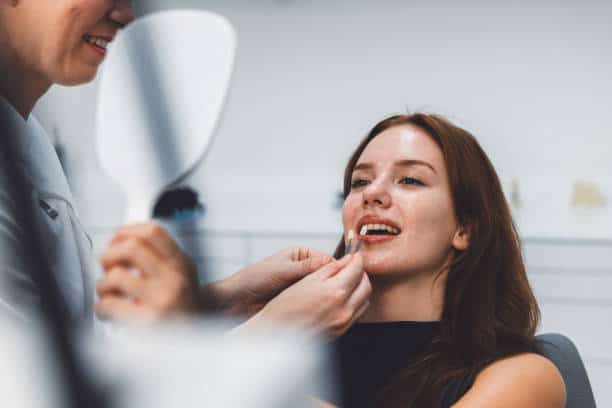 Patient getting dental veneers checked by dentist while holding a mirror in clinic.