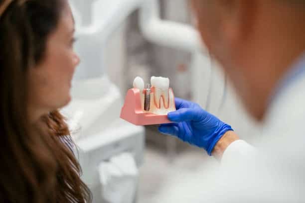 Dentist explaining dental implant model to patient, showcasing oral health and implant procedure.