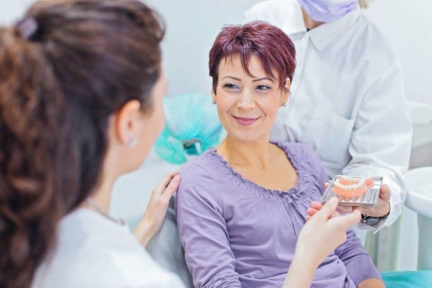 Woman in dentist's office discussing dental implants with professionals, showcasing dental care consultation.