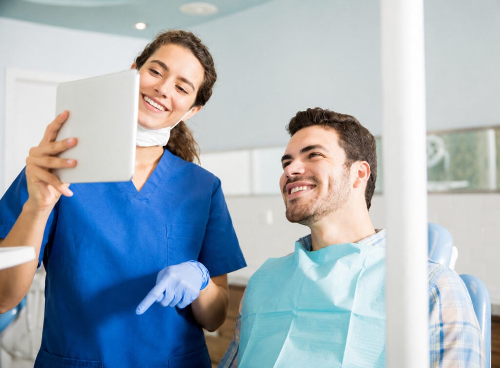 Persona che controlla la glicemia con un glucometro vicino a un misuratore di pressione e a una cartella medica su un tavolo.