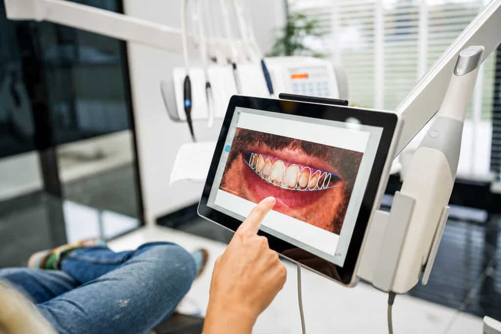 Dentist using digital tablet to analyze patient’s dental X-ray during consultation in modern clinic.