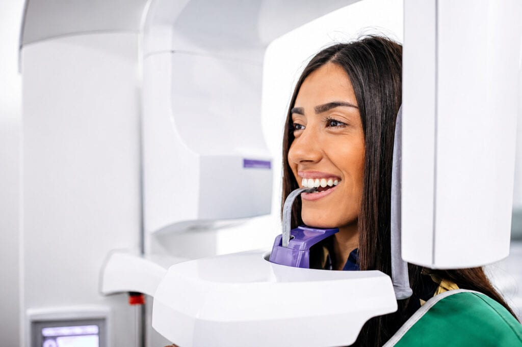 Woman smiling during a dental panoramic X-ray procedure in a modern clinic setting.